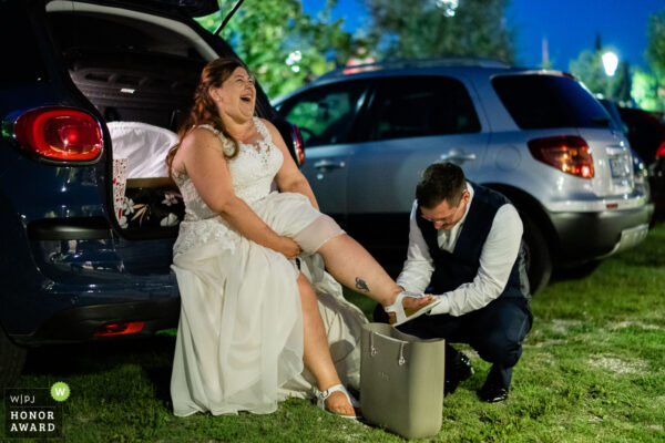 Lo sposo aiuta la sposa a cambiare le scarpe nel parcheggio del ristorante alla fine della festa